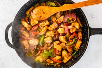 veggie and chicken mixture in a skillet with a wood spoon