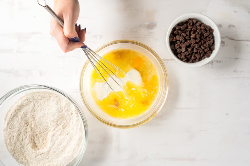 hand using a whisk to combine wet ingredients in a glass bowl