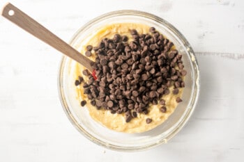 chocolate chips added to muffin batter in a glass bowl with a spatula