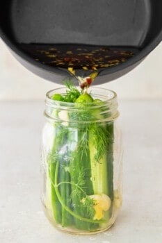 pouring brine into a glass jar filled with cucumber spears