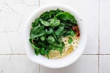 spinach, bacon, and cheese added to egg mixture in a white bowl