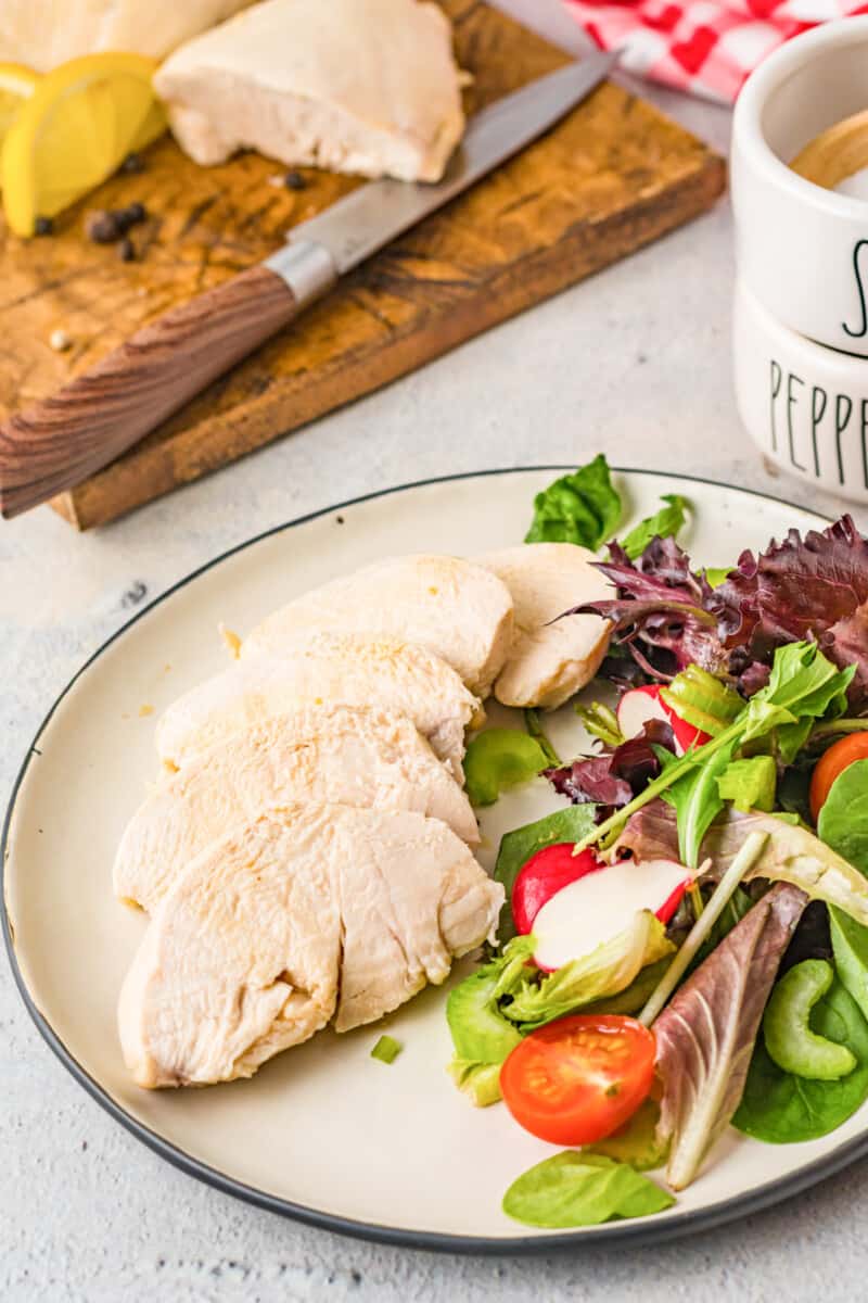 sliced poached chicken breast on a white plate with salad