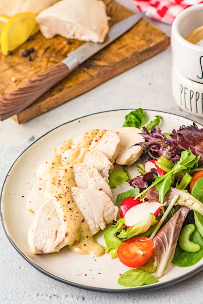 sliced poached chicken breast on a white plate with salad
