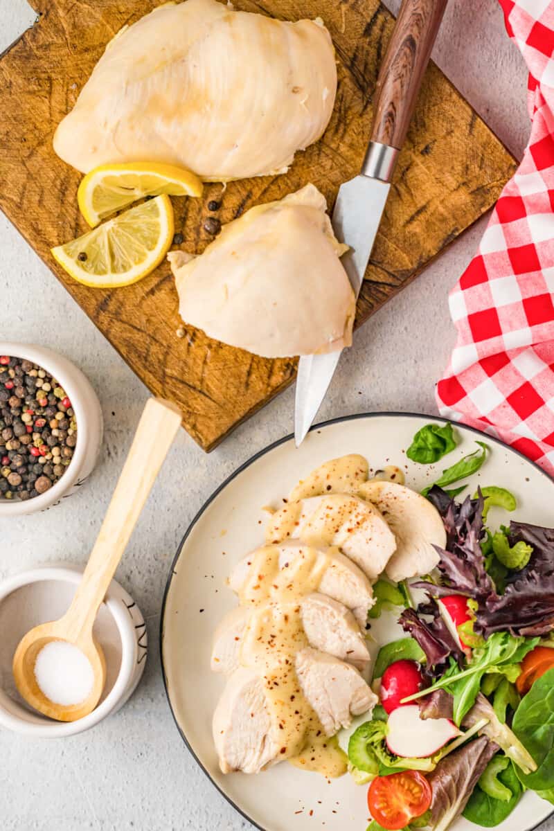 poached chicken breasts on a cutting board and on a plate with salad