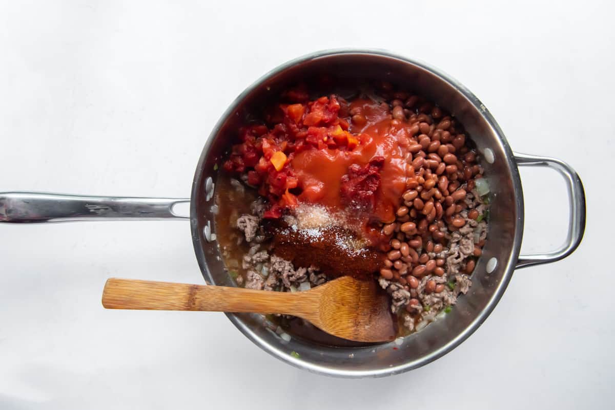 ingredients for chili in a pot with a wood spoon