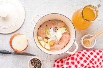 chicken breasts in a pot with bay leaf, salt, peppercorns, and sliced onion