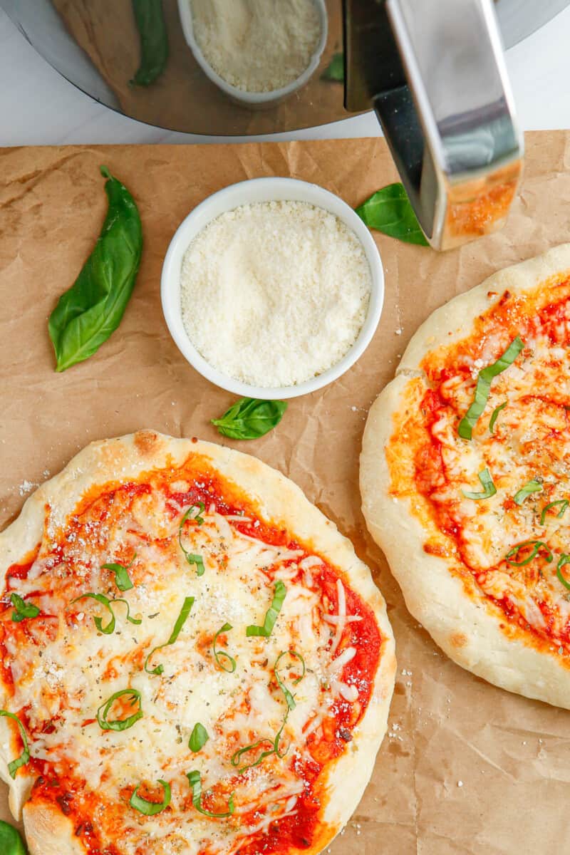 2 cheese pizzas on parchment paper with grated Parmesan cheese in a white bowl