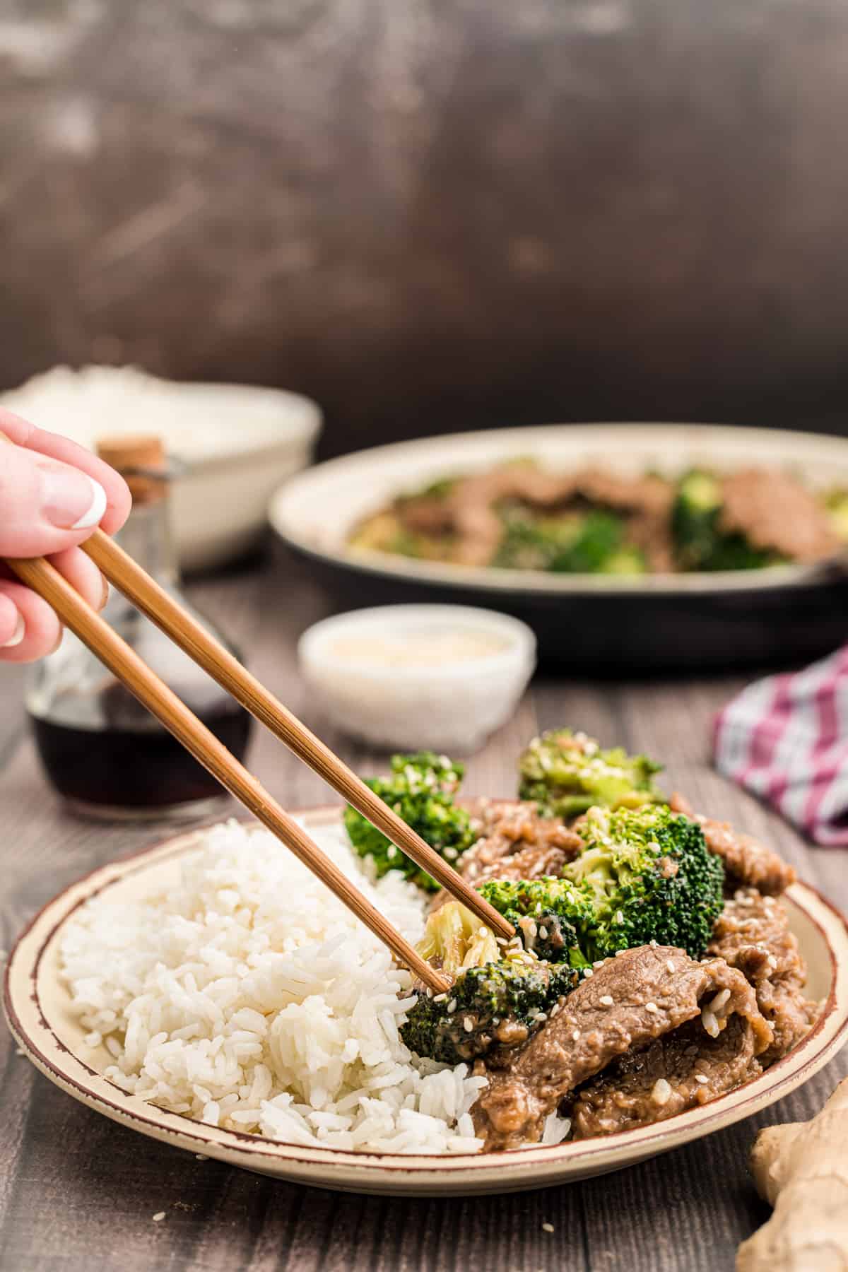 hand using chopsticks to grab a piece of broccoli off of a plate