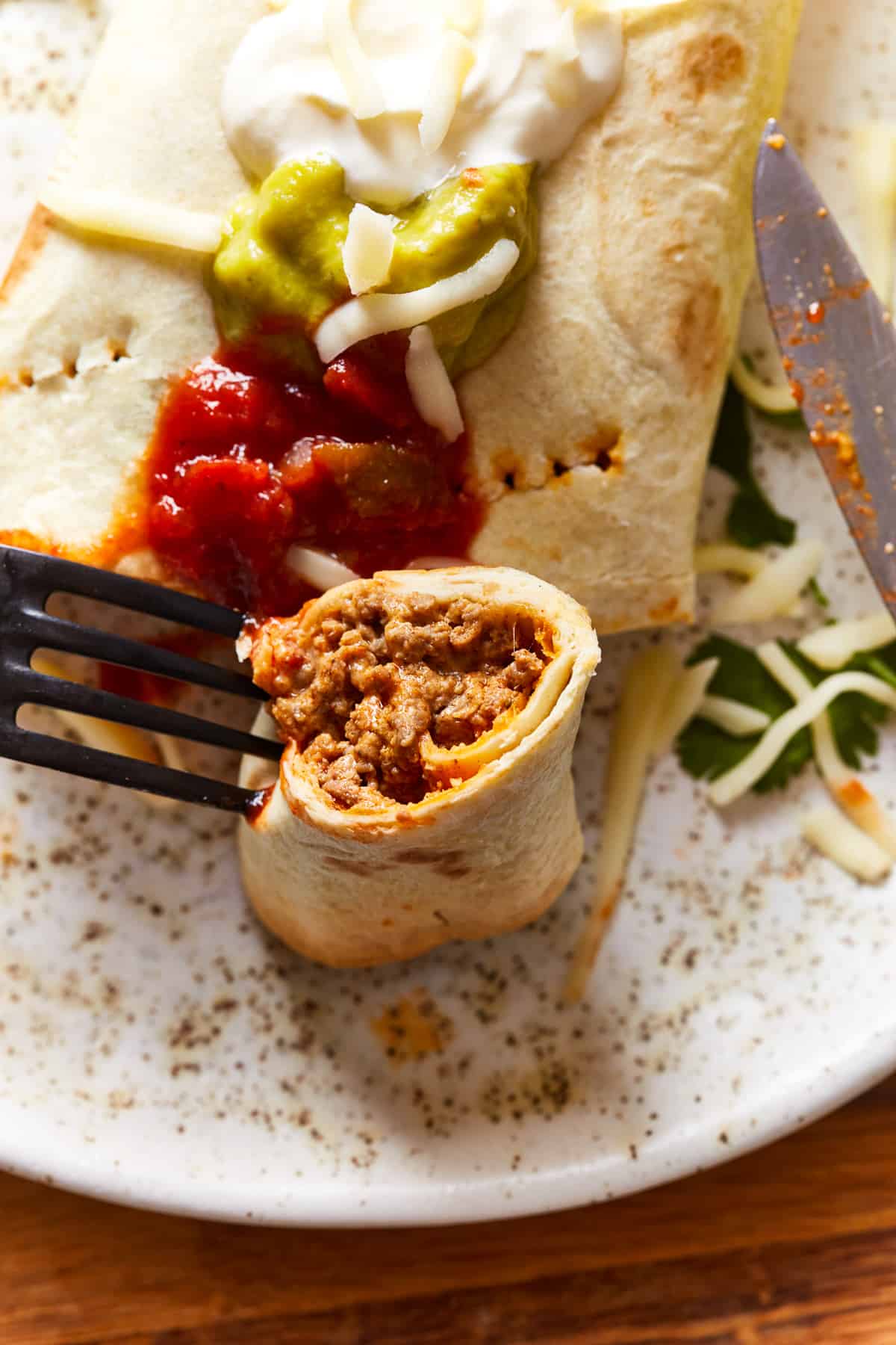 A fork holding a halved taquito upright to show the filling on a white plate.