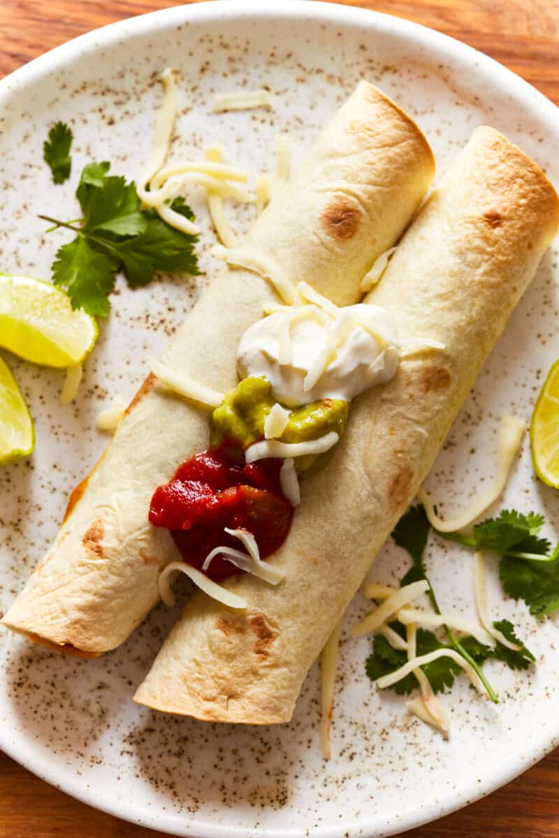 overhead view of 2 beef taquitos on a white plate.