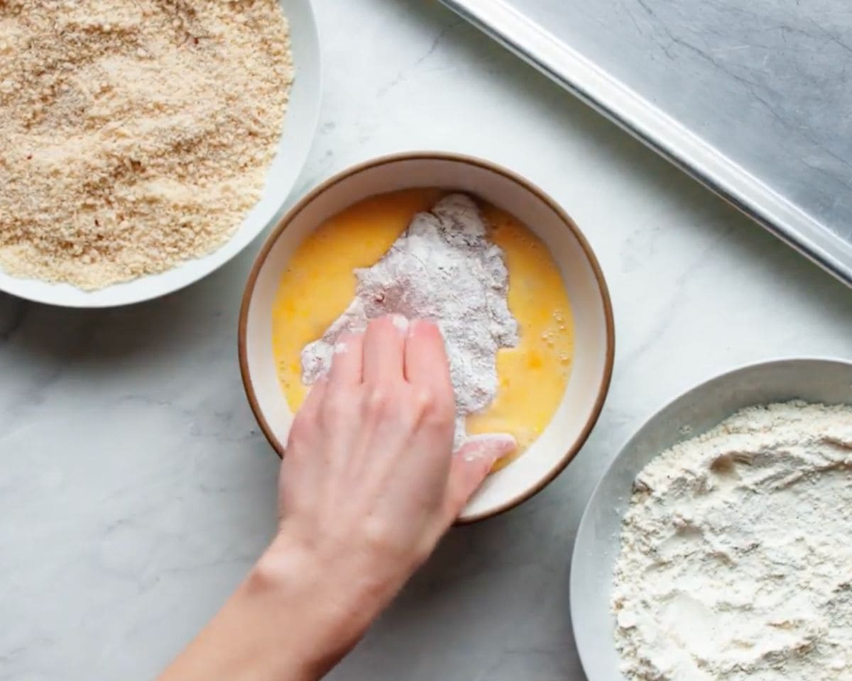 Raw chicken being dipped into egg wash during breading process for crispy baked chicken