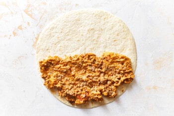 a flour tortilla with beef taquito filling laid on the bottom half.