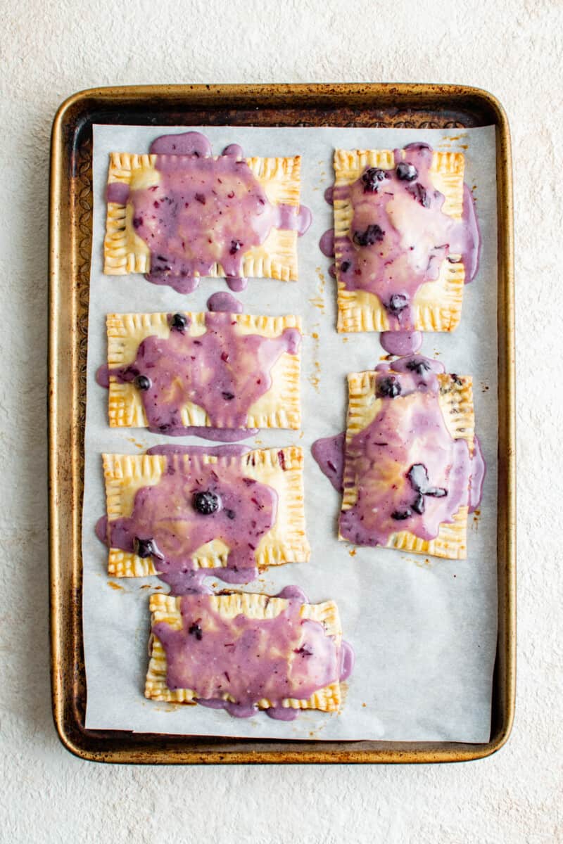 overhead view of 6 iced blueberry pop tarts on a baking sheet.
