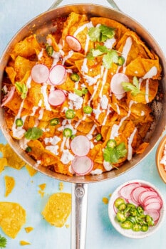 Overhead view of chilaquiles in a sauté pan with radishes and jalapeños.