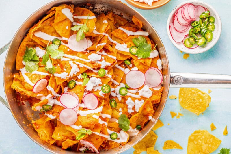 Overhead view of chilaquiles in a sauté pan with radishes and jalapeños.