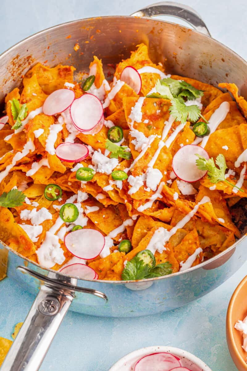 Chilaquiles in a sauté pan with radishes and jalapeños.