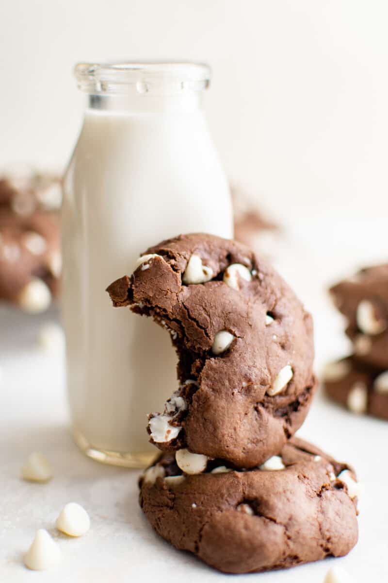 1 chocolate cake mix cookie missing a bite stacked on another cookie leaning against a carafe of milk.