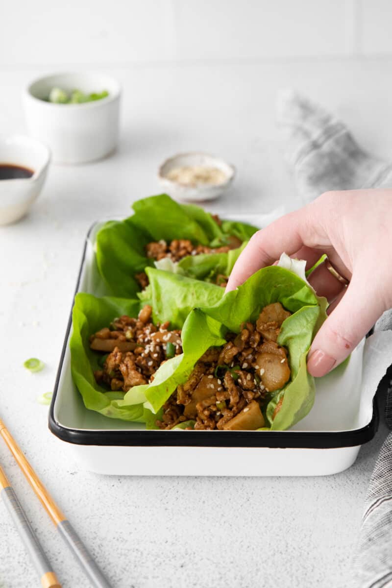 a hand grabbing a pf changs lettuce wrap from a white tray.