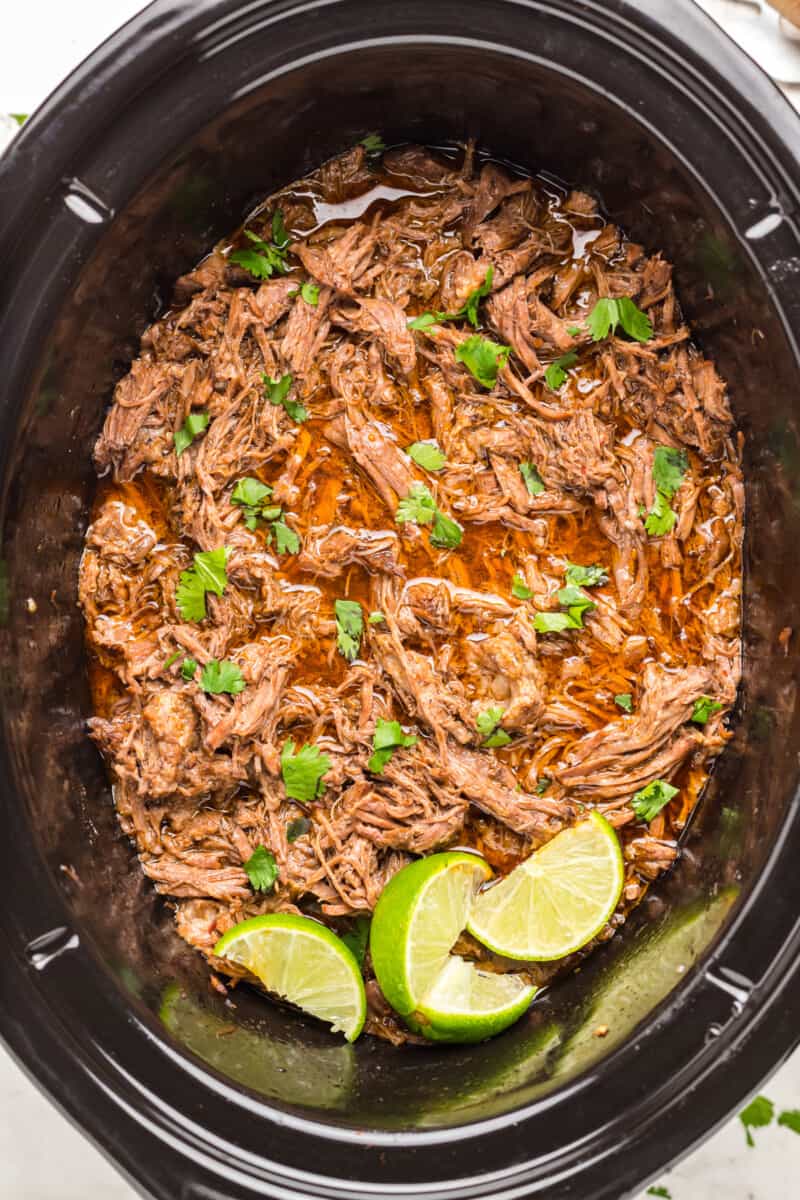 barbacoa beef in a crockpot with limes.