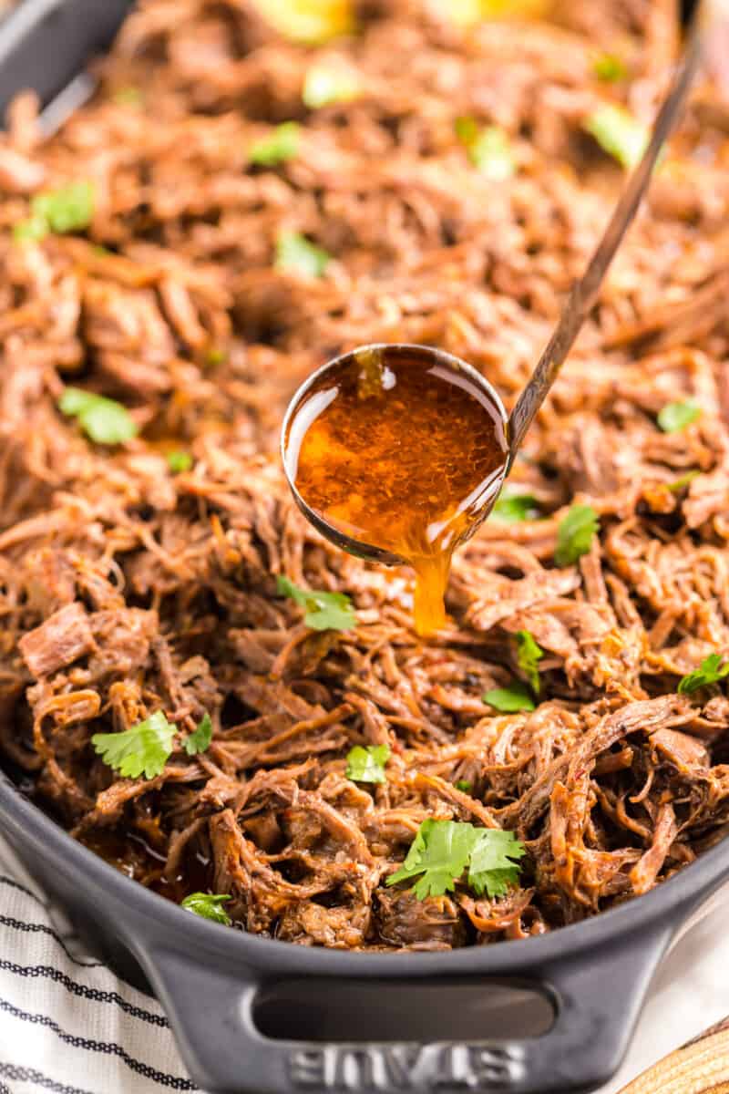 close up of barbacoa beef with a ladle of drippings.