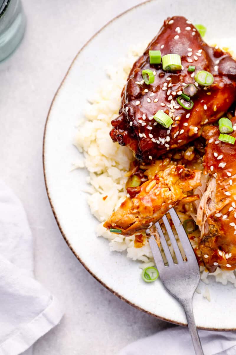 honey garlic chicken on top of rice on a white plate with a fork