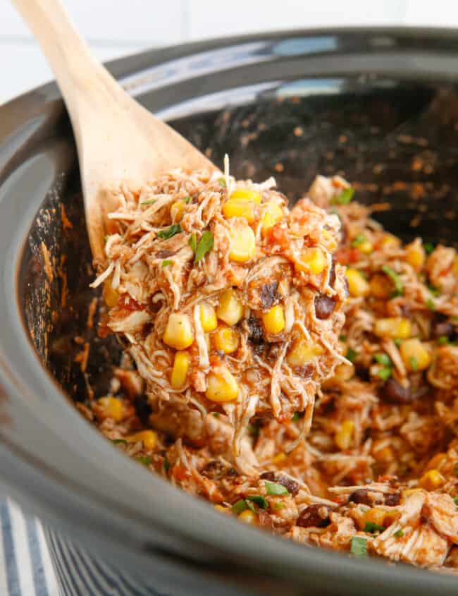 close up of crockpot mexican shredded chicken in a crockpot with a wooden spoon.