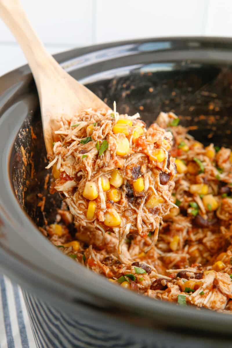 close up of crockpot mexican shredded chicken in a crockpot with a wooden spoon.