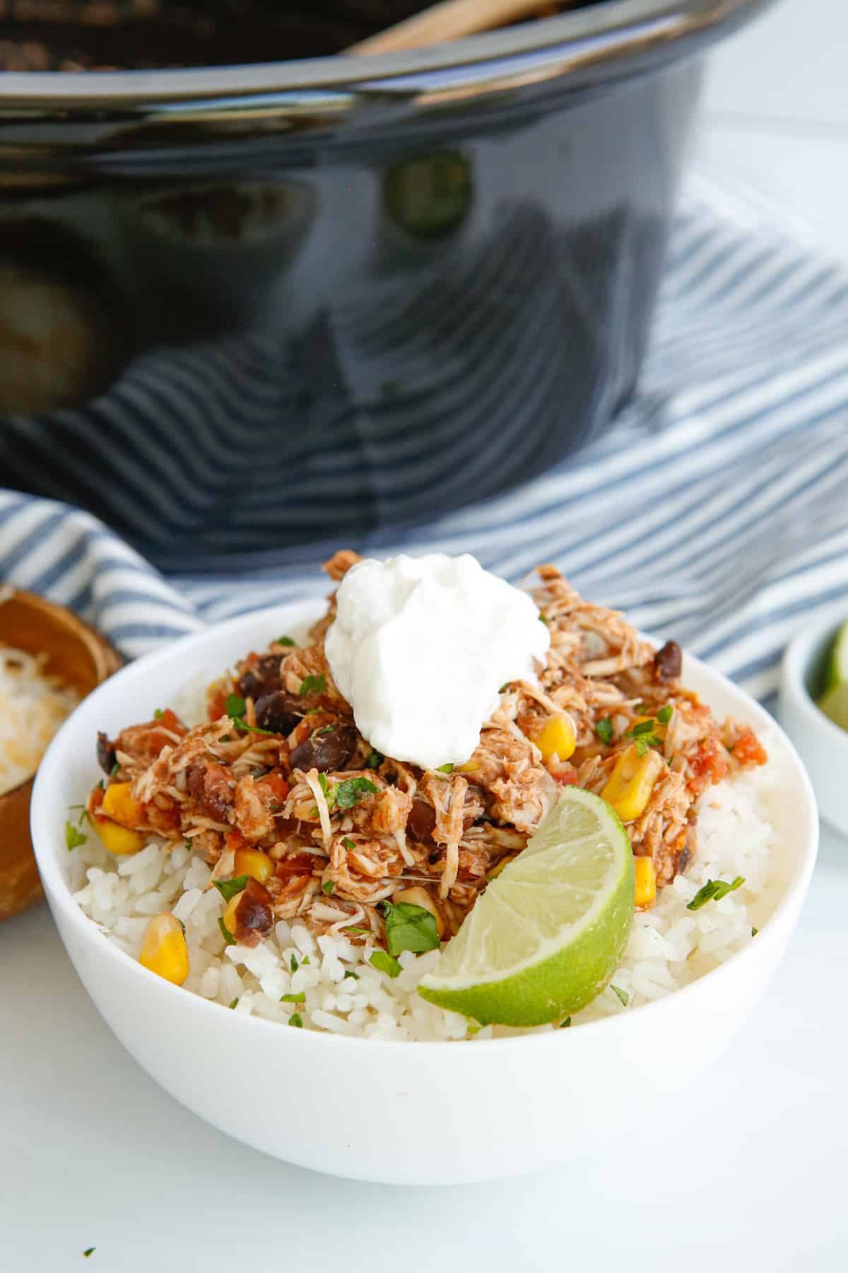 crockpot mexican shredded chicken over rice in a white bowl with sour cream.