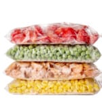 A stack of plastic bags filled with different kinds of vegetables.