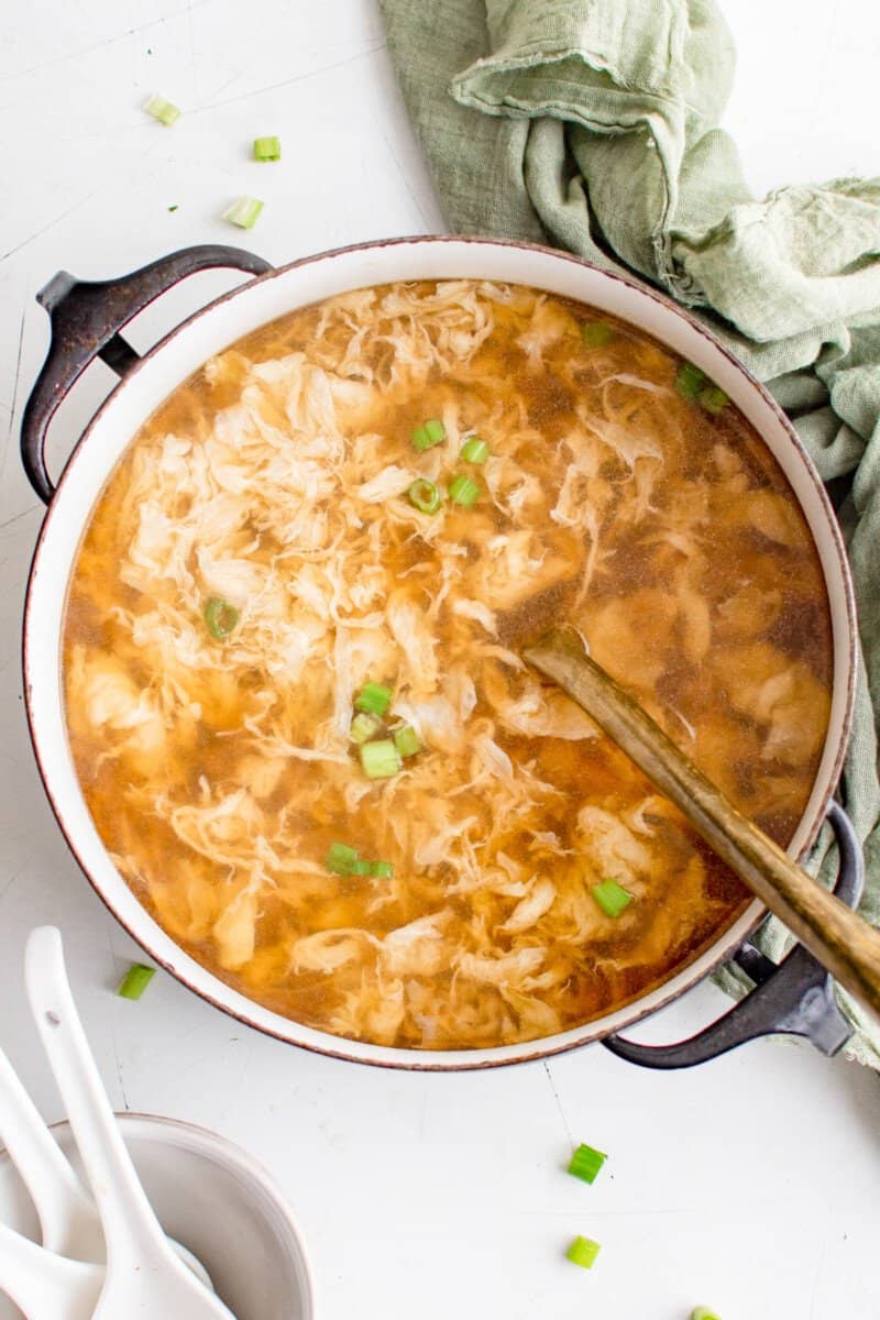 overhead view of egg drop soup in a black pot with a spoon.