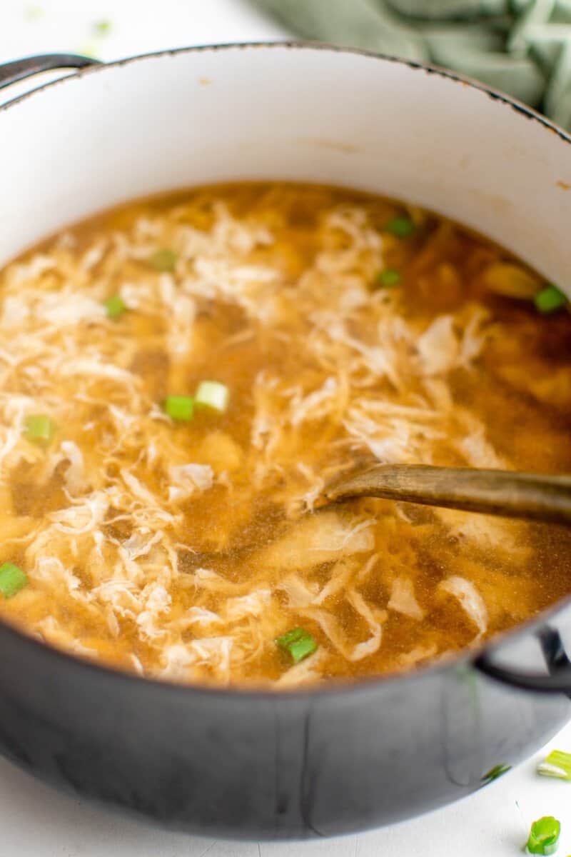 close up view of egg drop soup in a black pot with a spoon.