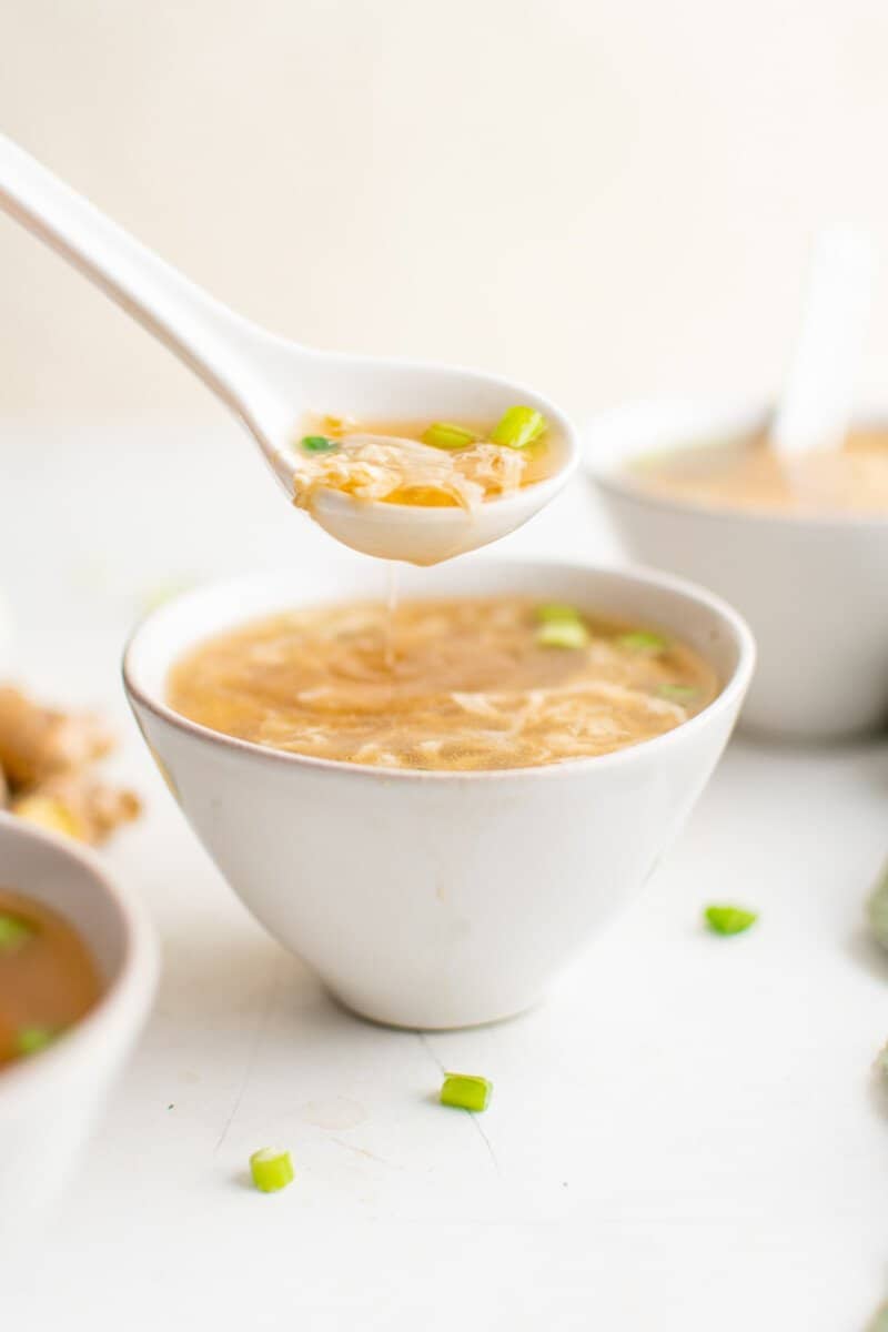 a spoonful of egg drop soup suspended over egg drop soup in a white bowl.