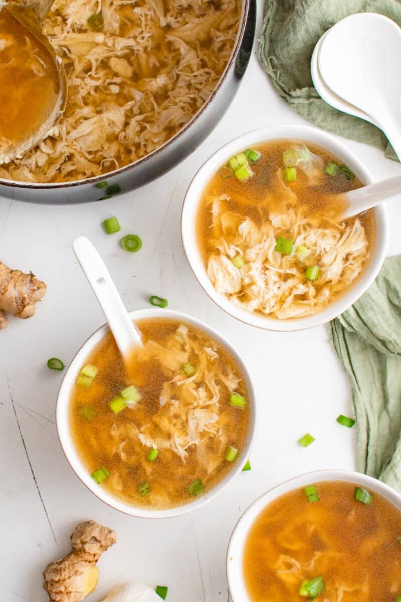 3 bowls of egg drop soup next to egg drop soup in a black pot.