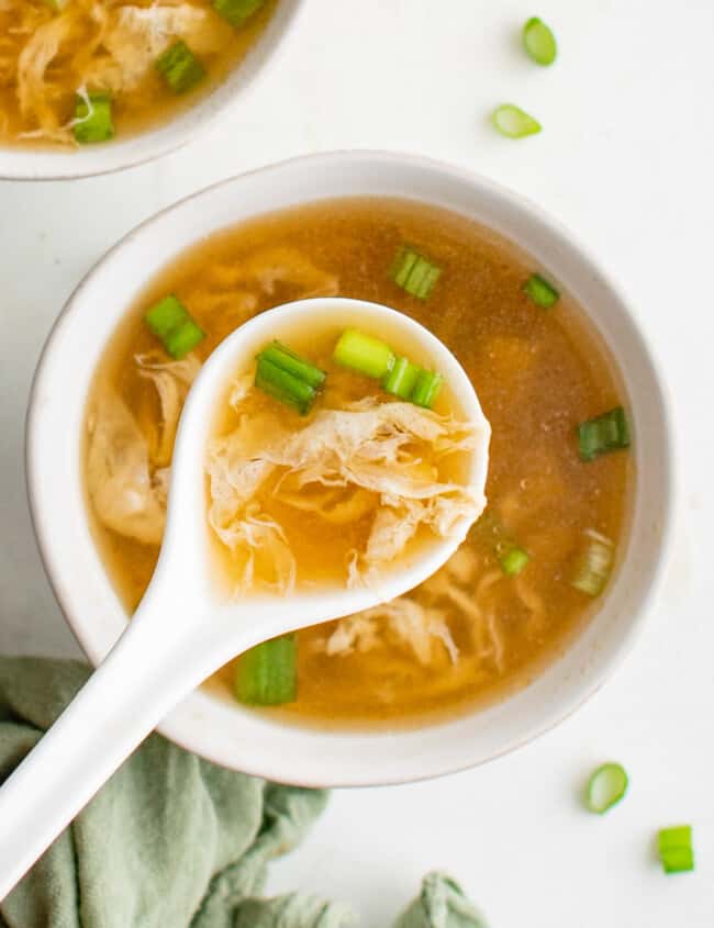 overhead view of egg drop soup in a white bowl with a white spoon.