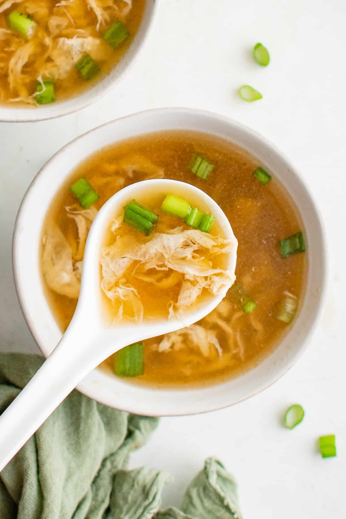 overhead view of egg drop soup in a white bowl with a white spoon.