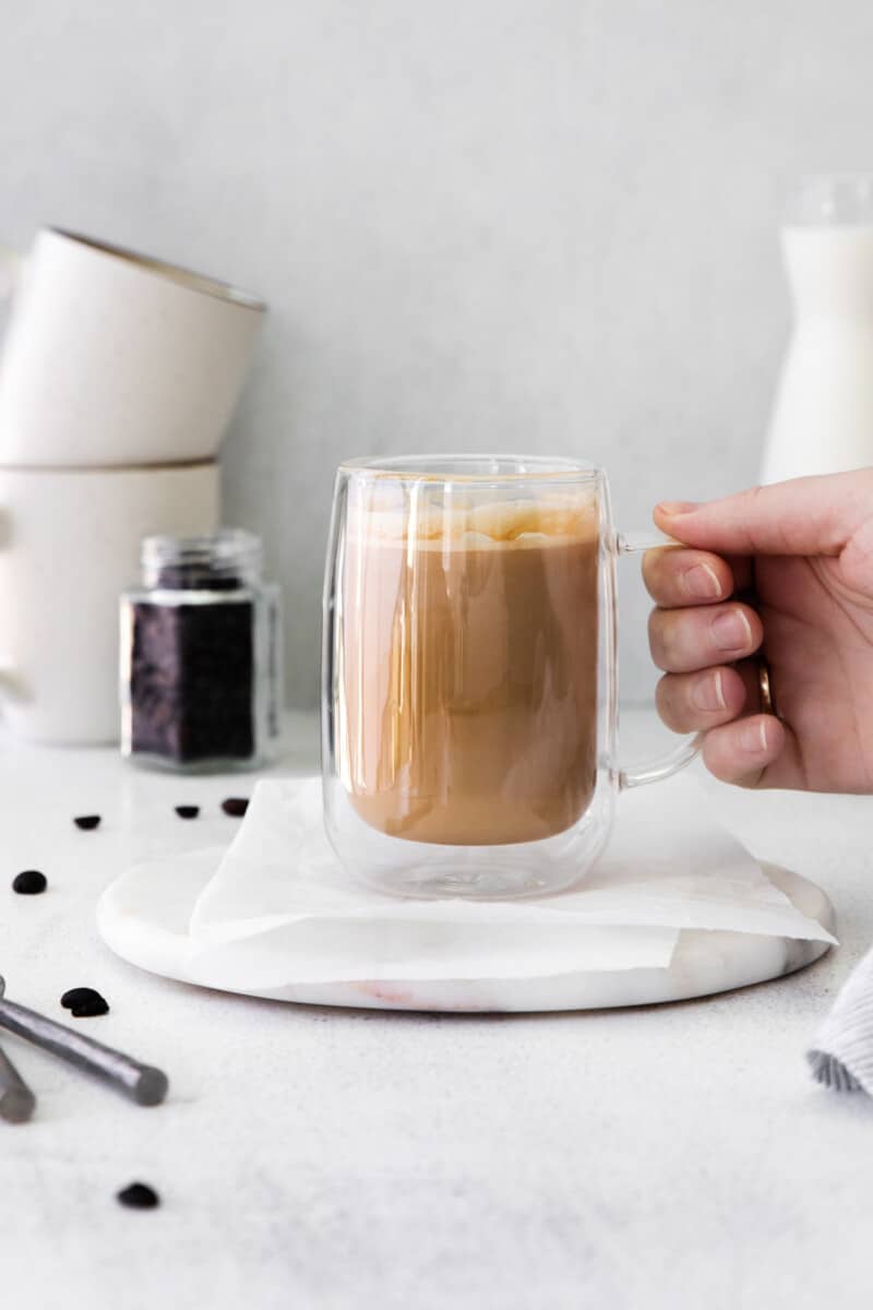 flat white drink in a glass mug with a hand holding the mug
