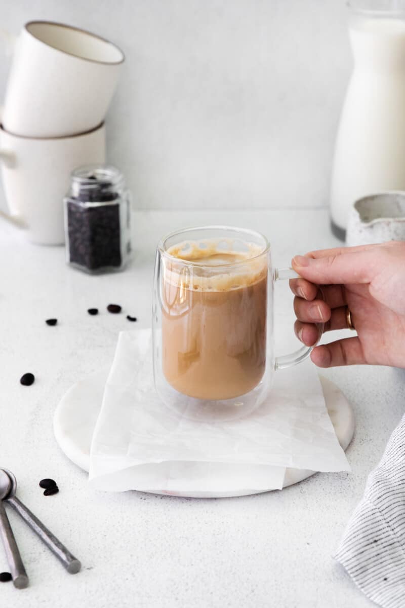 flat white drink in a glass mug with a hand holding the mug