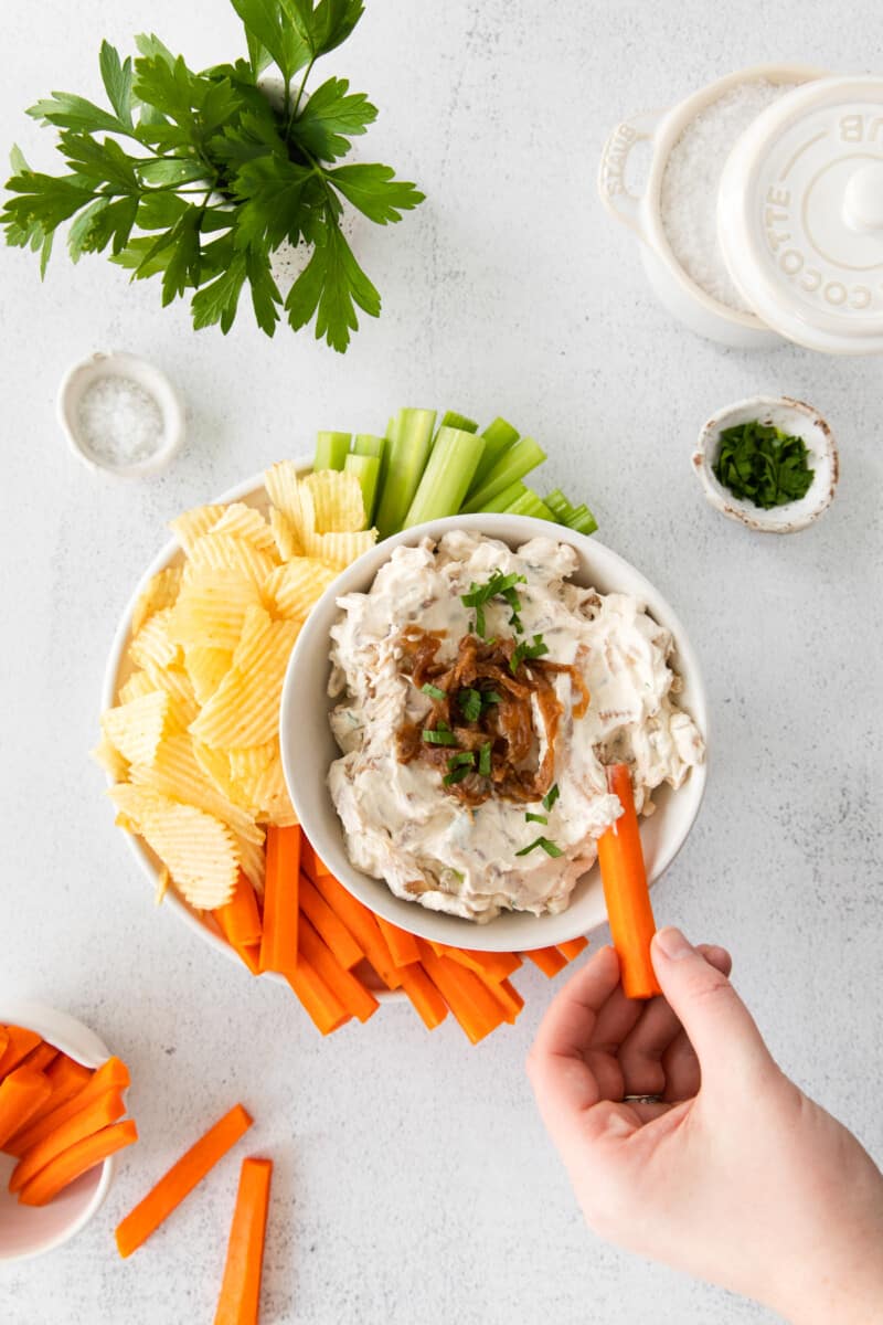 hand dipping a carrot stick into a bowl of french onion dip