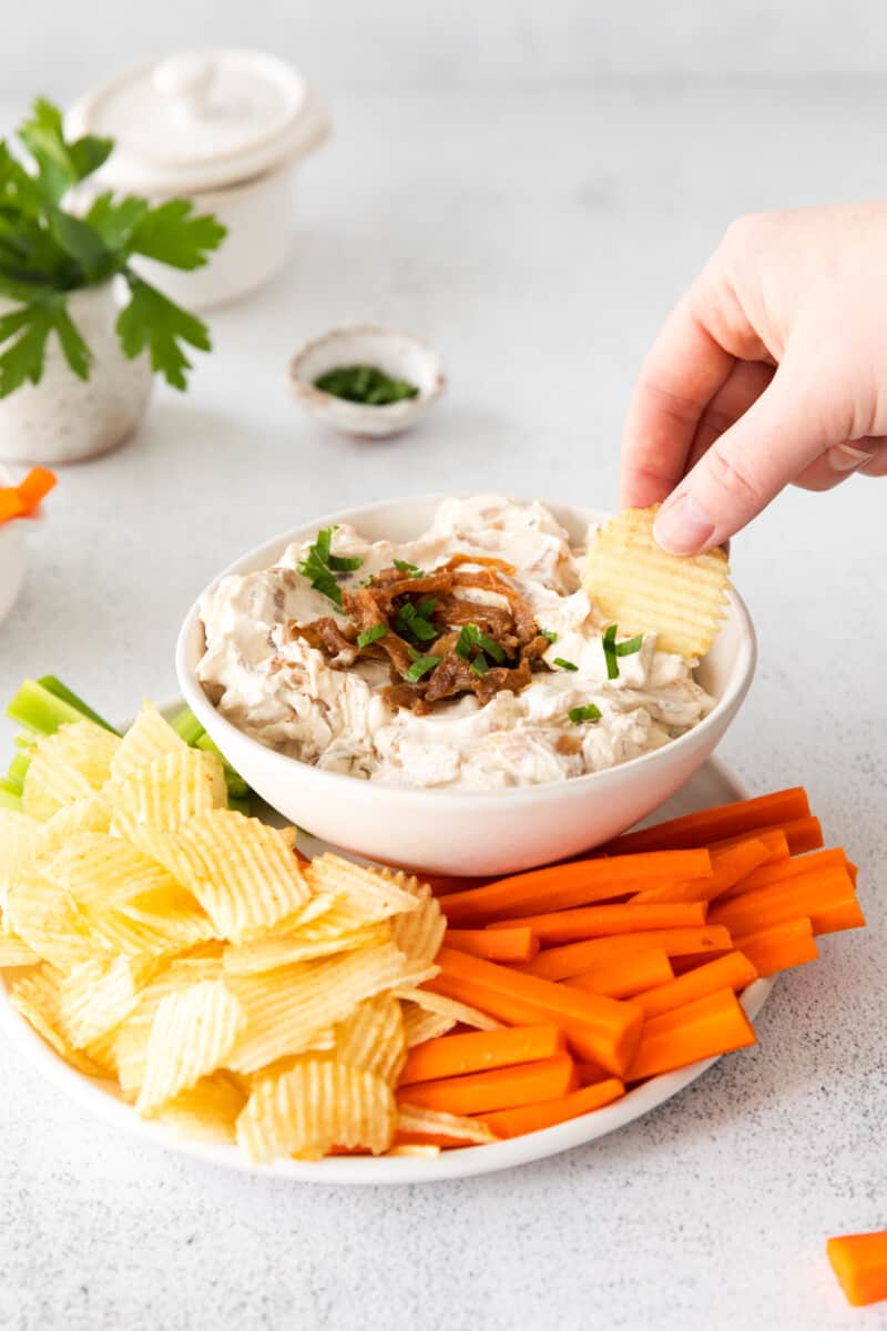 hand dipping a chip into a bowl of french onion dip