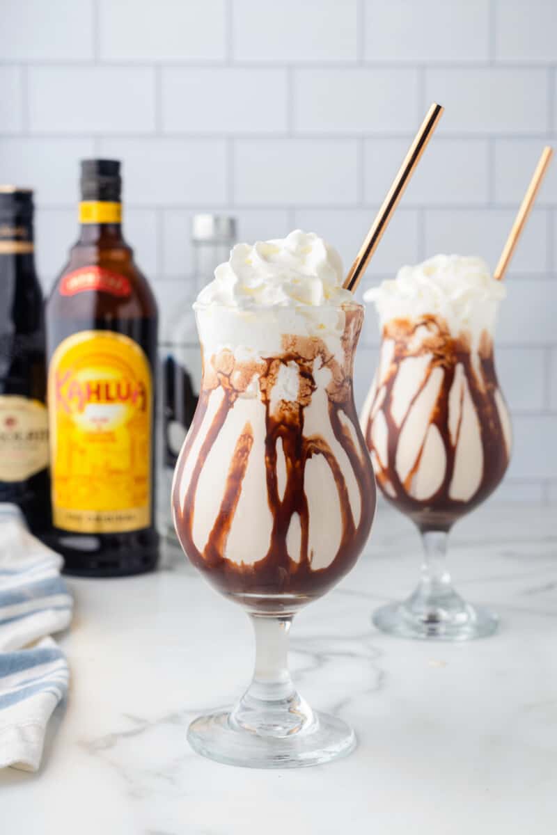 2 frozen mudslides with gold straws in front of bottles of alcohol.
