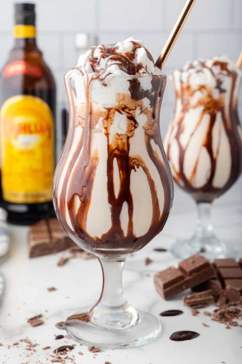 close up view of 2 mudslides with gold straws in front of bottles of alcohol.