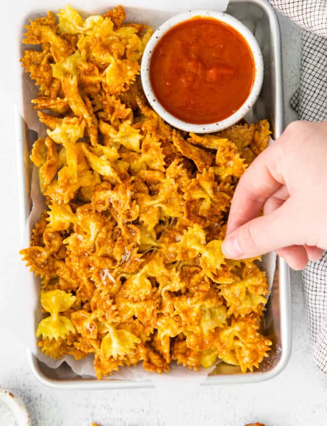 a hand grabbing a garlic parmesan pasta chip from a platter with marinara sauce.