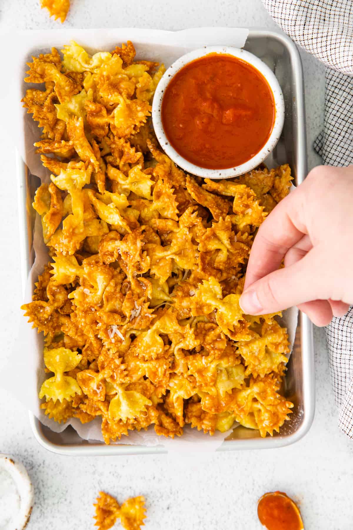 a hand grabbing a garlic parmesan pasta chip from a platter with marinara sauce.