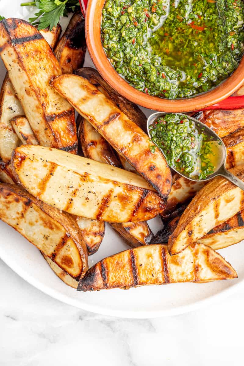 overhead view of grilled potato wedges with chimichurri on a white plate.