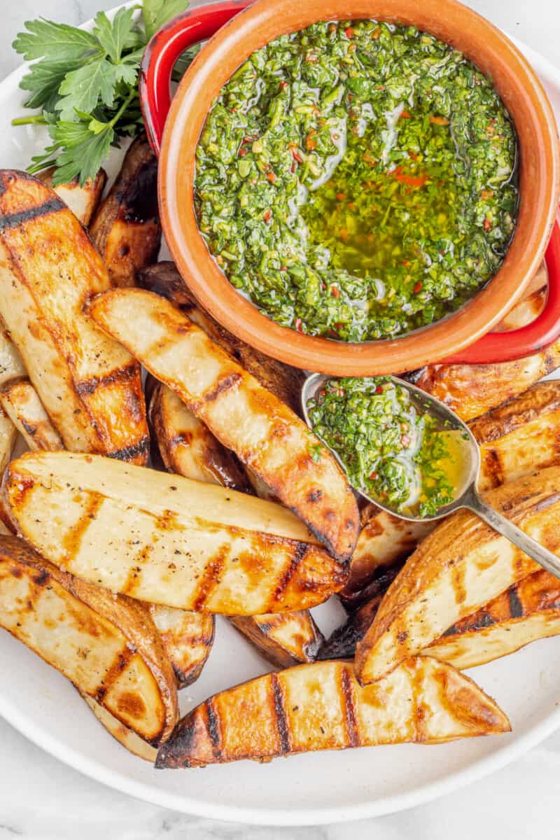 overhead view of grilled potato wedges with chimichurri on a white plate.