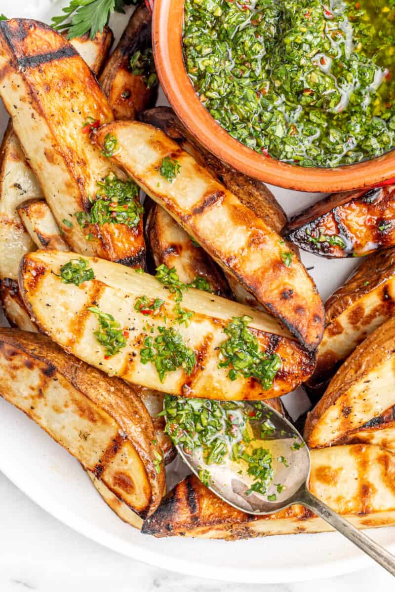 overhead view of grilled potato wedges with chimichurri on a white plate with a spoon.
