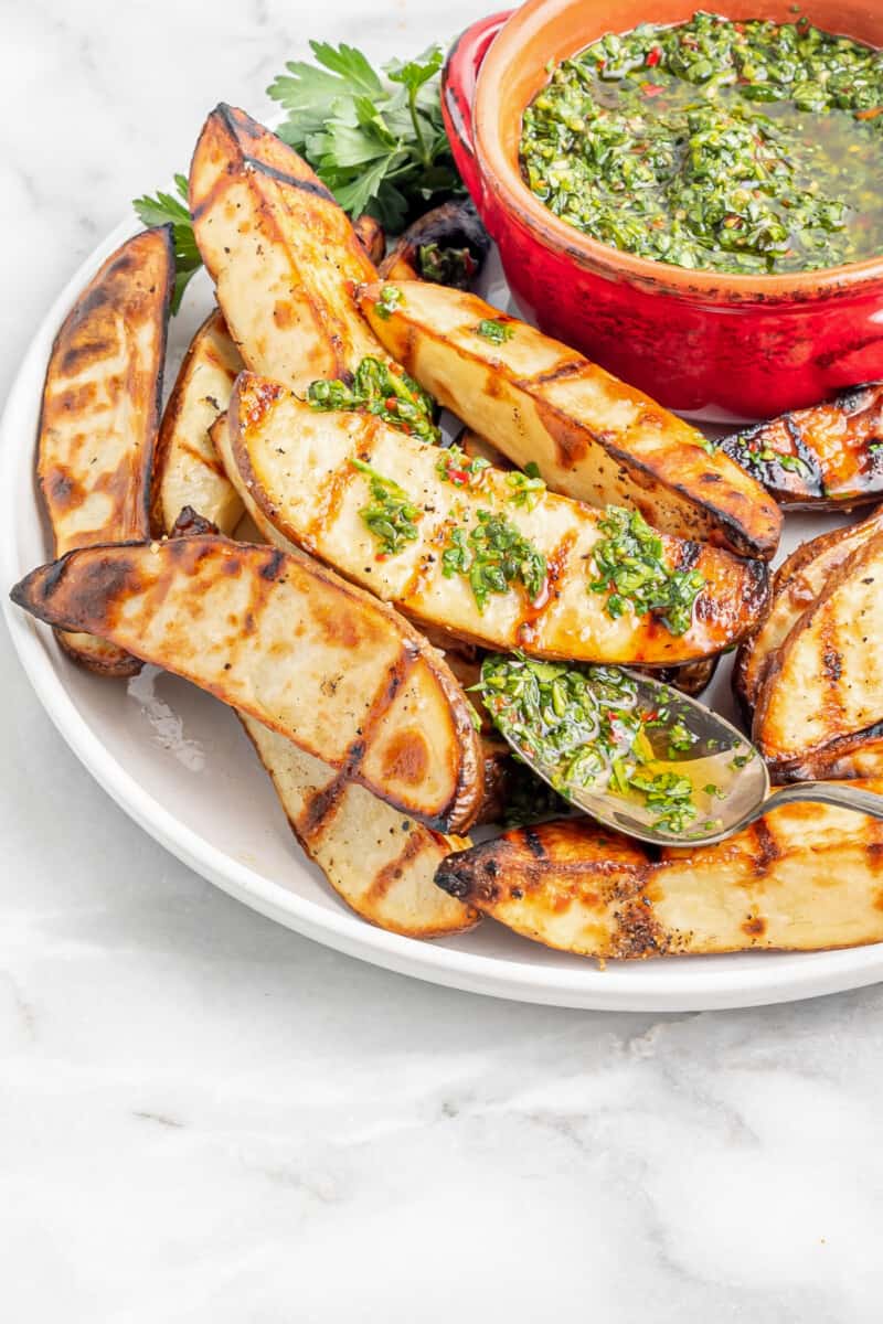 fatias de batata grelhadas com chimichurri em um prato branco com uma colher.