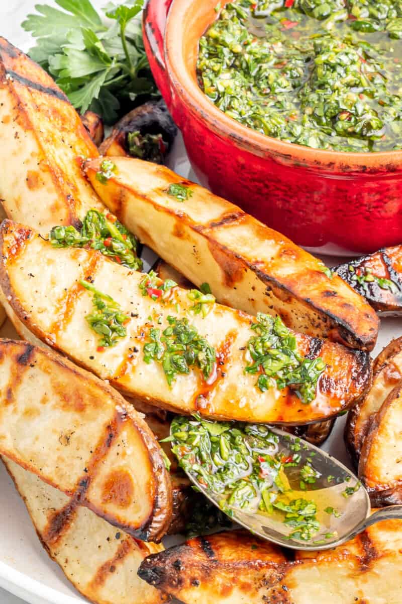 fatias de batata grelhadas com chimichurri em um prato branco com uma colher.