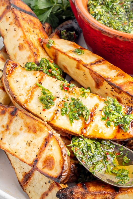 close up of grilled potato wedges with chimichurri with a spoon.