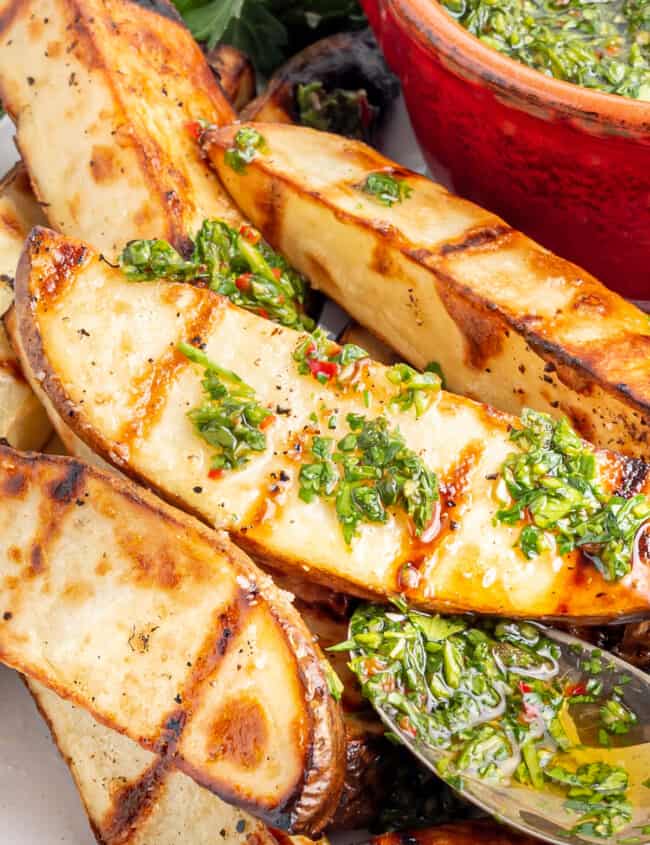 close up of grilled potato wedges with chimichurri with a spoon.